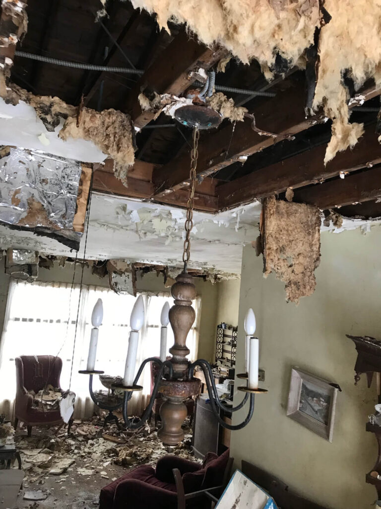 A room with damaged ceiling and a broken chandelier due to water leakage