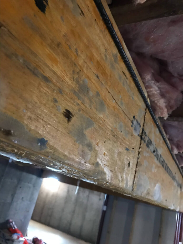 A wooden beam with a pipe attached, showing signs of mold.
