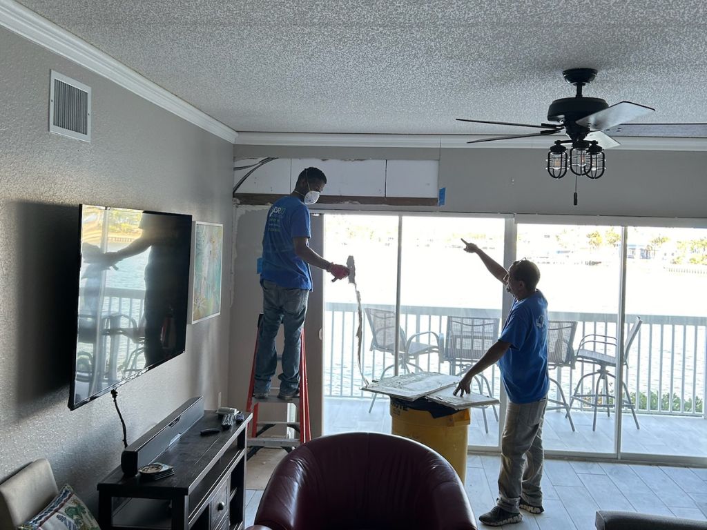 Two Workers Repairing Drywall In A Living Room.