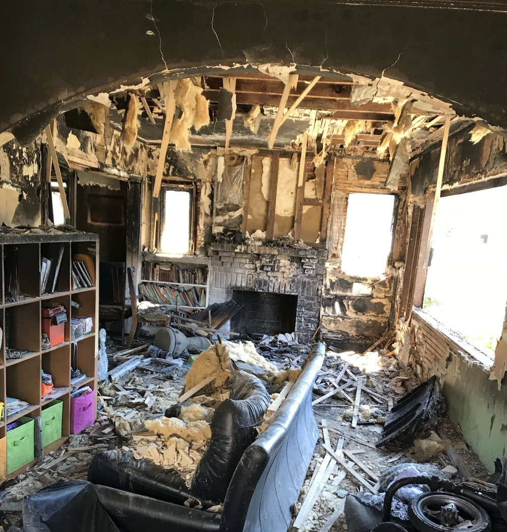 A Fire-Damaged Living Room Featuring A Charred Couch And Partially Burned Bookshelves.